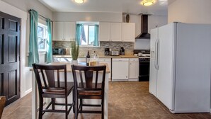 A compact kitchen with white cabinets, a white refrigerator, and a dining area with two wooden chairs. - 4 BD Entire House Located Close to Downtown and Little Italy! (San Diego)