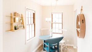 Uma sala de jantar com uma mesa azul, cadeiras brancas e prateleiras com objetos decorativos.