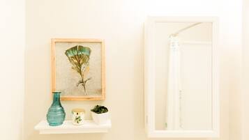 Une salle de bain avec une œuvre d’art encadrée, un vase turquoise, un petit récipient blanc et une étagère blanche.