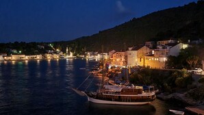 Un poble a la costa de nit, amb un vaixell amarrat, edificis al llarg de la riba i un turó al fons.