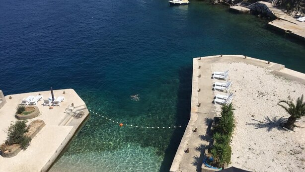 Un hotel a la vora de la platja amb aigües cristal·lines, una piscina i gandules.