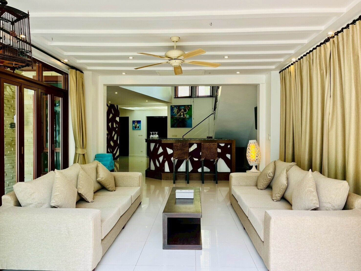A spacious living area with two sofas, a coffee table, a ceiling fan, and a view of the dining area.