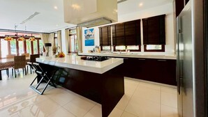 Uma cozinha moderna com uma ilha grande, armários escuros e uma geladeira de aço inoxidável.