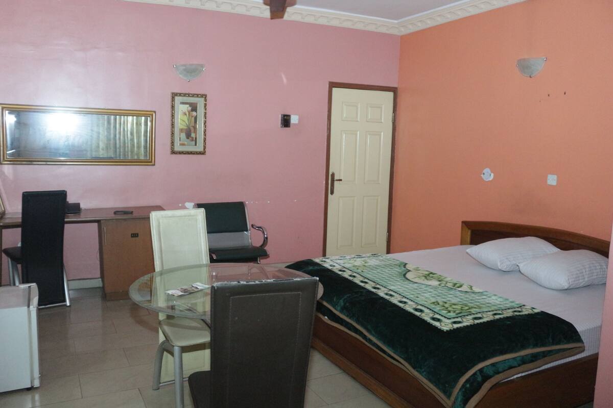 A bedroom with a bed, a desk, a chair, and a small table.