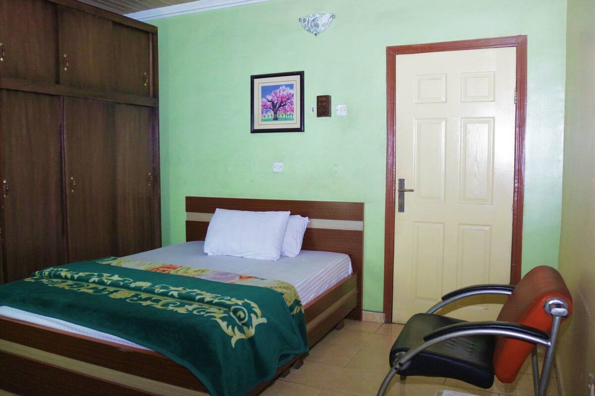 A bedroom with a bed, a wooden wardrobe, a door, and a chair.