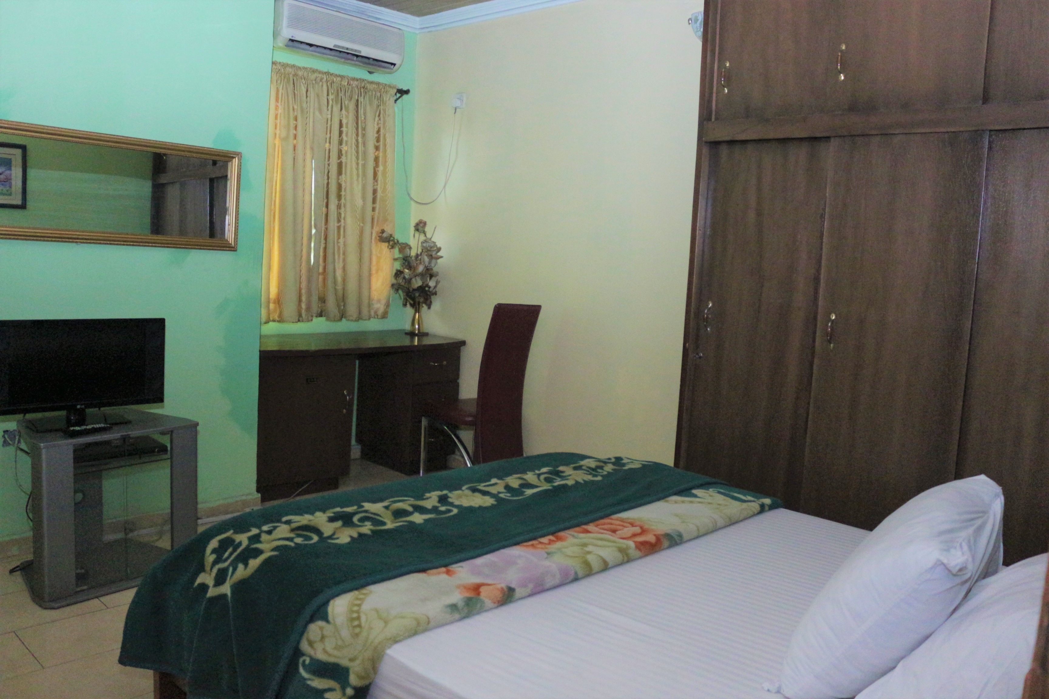 A bedroom with a bed, a desk, a chair, a television, and a wardrobe.