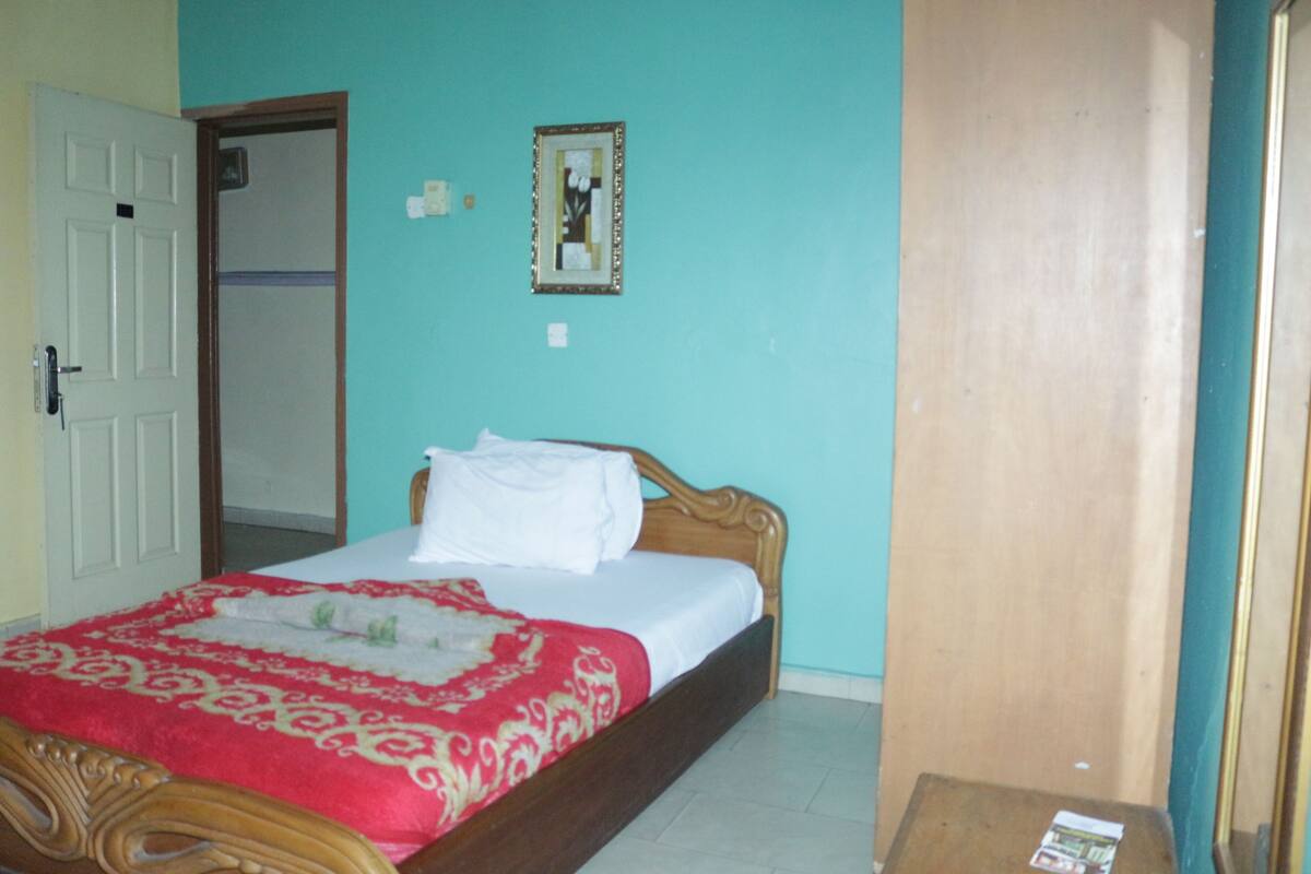 A bedroom with a bed, a door, a mirror, and a small table.