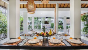 A dining area with a long table set for six, surrounded by large windows and a view of a garden. - Beautiful 4 Bedroom Villa, Oberoi (Seminyak)