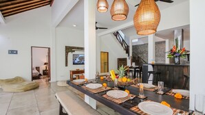 A modern dining area with a long table set for four, featuring woven placemats and a central vase with flowers. - Beautiful 4 Bedroom Villa, Oberoi (Seminyak)