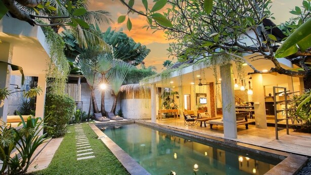 A poolside area with a clear view of the pool, surrounded by lush greenery and a thatched-roof structure. - Beautiful 4 Bedroom Villa, Oberoi (Seminyak)