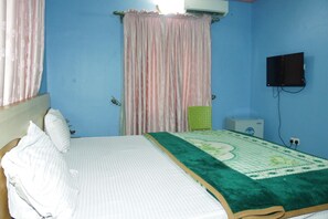 A bedroom with a bed, curtains, a television, and a small table. - Chisam Suites Annex (Port Harcourt)