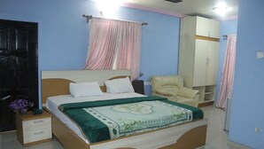 A bedroom with a bed, a nightstand, a chair, a wardrobe, and a door. - Chisam Suites Annex (Port Harcourt)