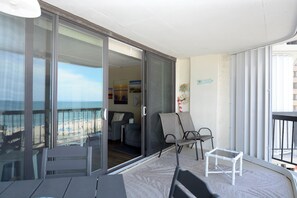 Un balcone con una porta vetrata che si apre su un soggiorno, un tavolino e due sedie.