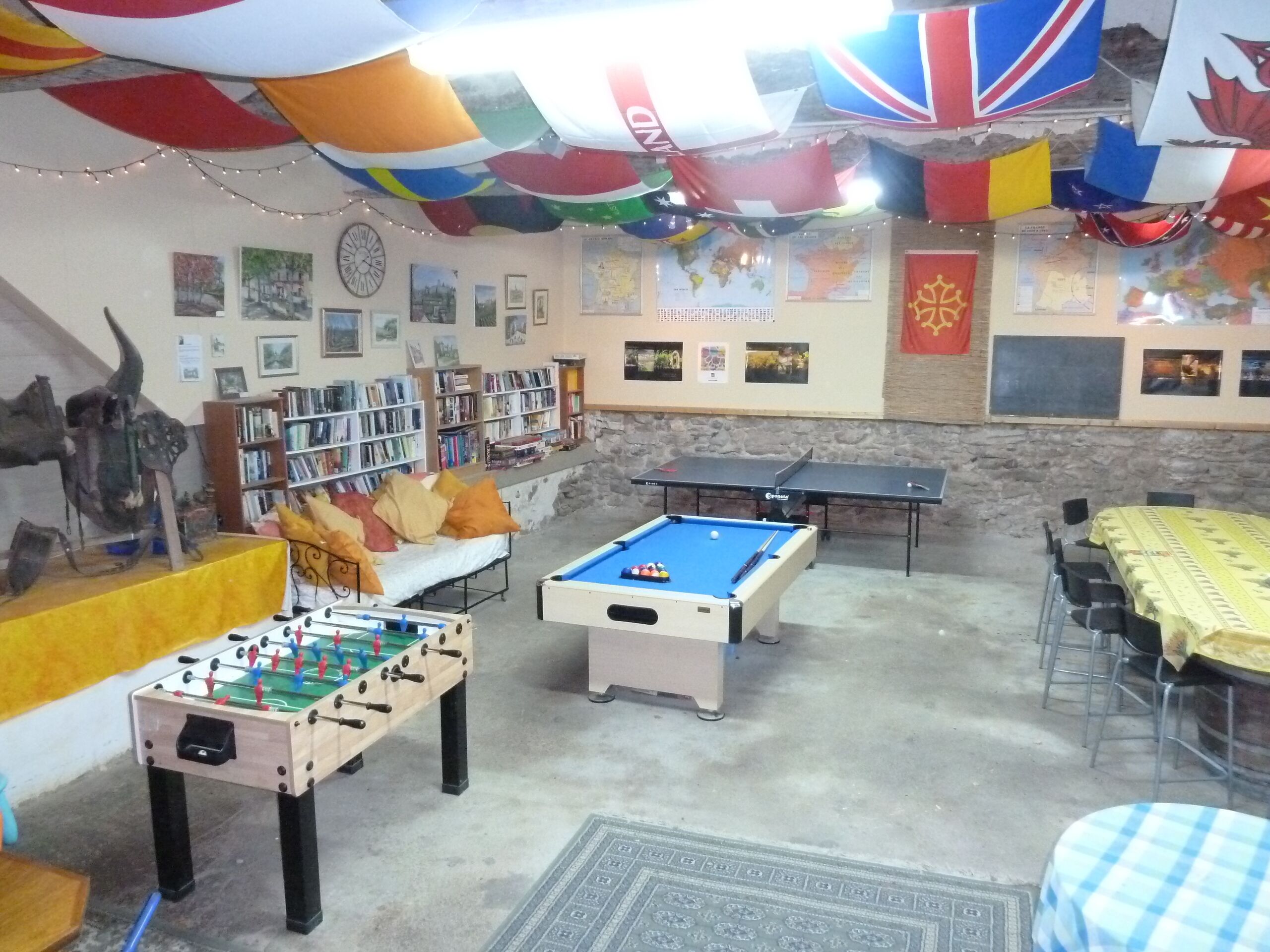 A room with a foosball table, pool table, and a sofa. There are bookshelves and a map on the walls.