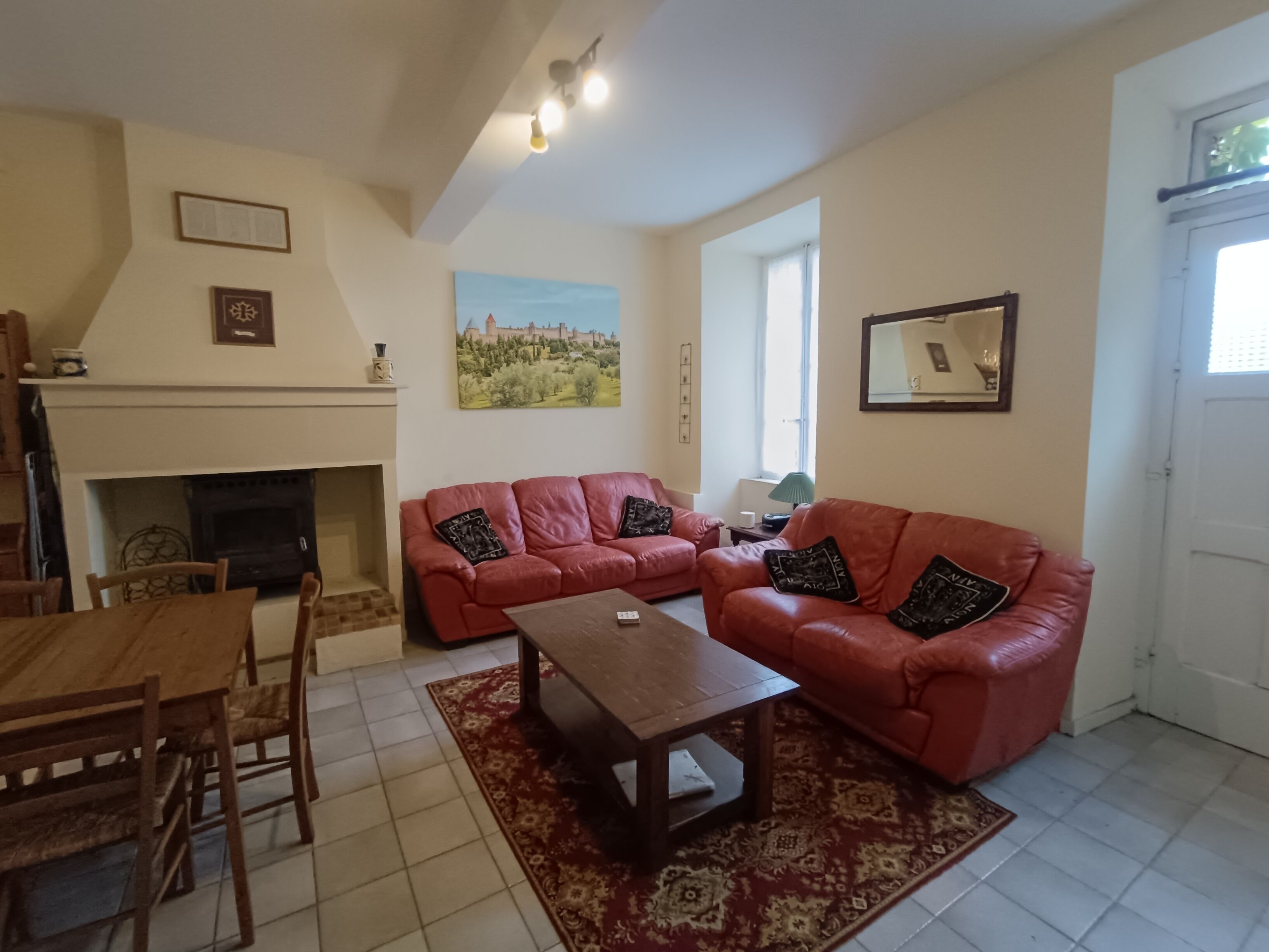 A living room with a fireplace, red leather sofas, a wooden coffee table, and a dining area with a table and chairs.