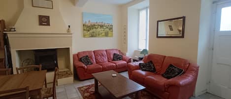 A living room with a fireplace, red leather sofas, a wooden coffee table, and a dining area with a table and chairs.