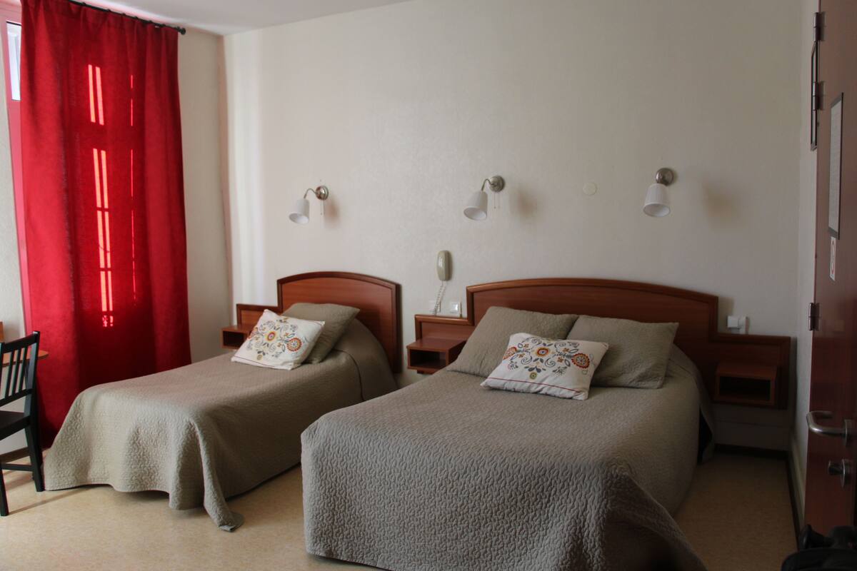 A hotel room with two single beds, a wooden nightstand, a chair, and a red curtain.