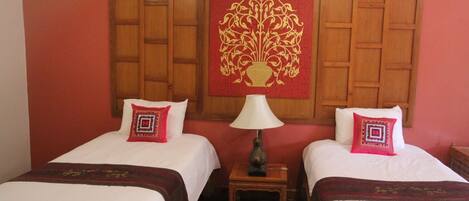 Habitación de hotel con dos camas, cada una con almohada roja y blanca, cabecero de madera y un tapiz decorativo rojo.