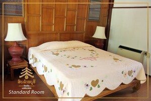 Habitación estándar con cabecera de madera, dos mesitas de noche con lámparas y una cama con colcha estampada.