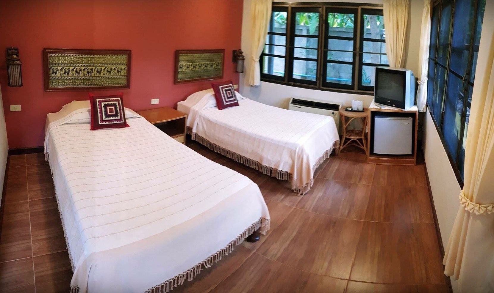 A hotel room with two beds, a television, and a window with curtains.