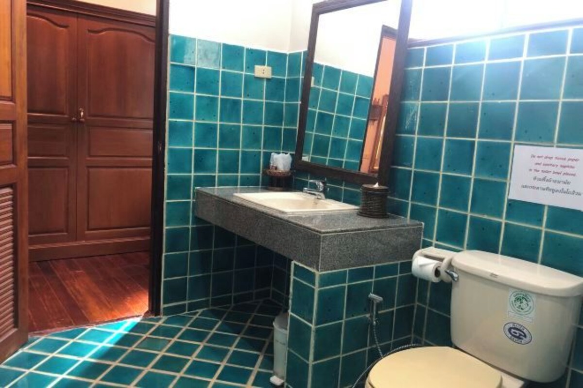 Une salle de bain équipée d’un lavabo, d’un miroir et de toilettes, avec des carreaux de couleur turquoise et des portes en bois.