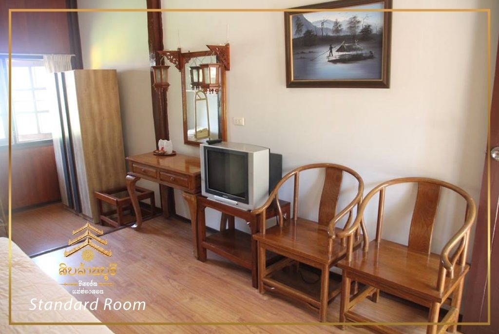 A standard room with wooden furniture, a television on a stand, a painting on the wall, and a window with curtains.