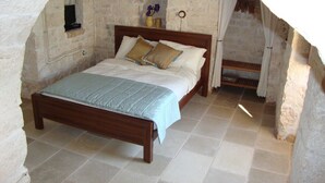 Ein Schlafzimmer mit einer Steinwand, einem hölzernen Bett und einem kleinen Fenster.