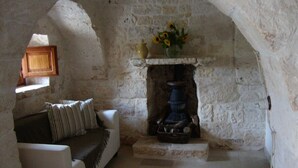 Ein gemütliches Zimmer mit Kamin aus Stein, einer Couch mit gestreiften Kissen und einer Vase mit Blumen auf dem Kaminbrett.