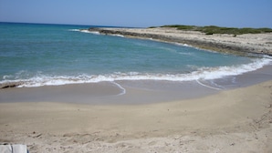 Ein Strand mit klarem, blauem Wasser, sandigem Ufer und Felsen.