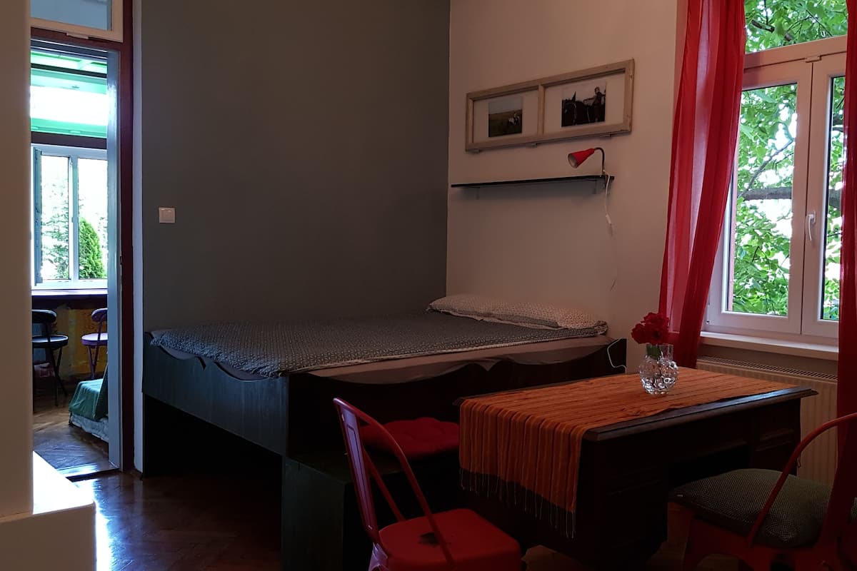 Una habitación pequeña y acogedora con una cama individual, un escritorio con silla y una ventana con cortinas rojas.