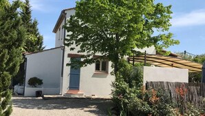 Una casa de dos pisos con fachada blanca, una puerta azul y un árbol grande en el frente.