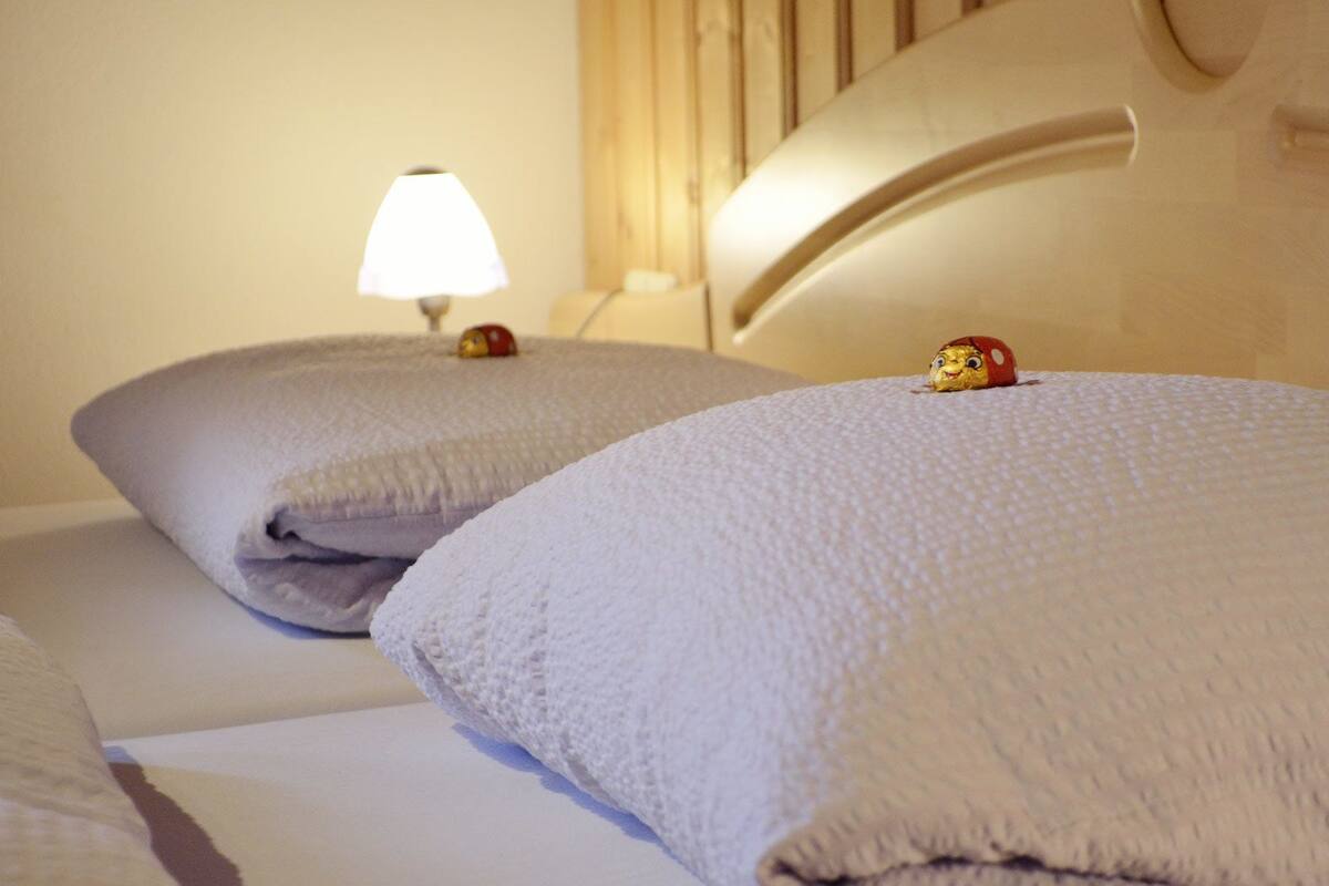Two beds with white linens and a lamp on a bedside table.