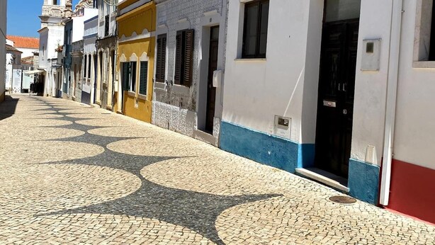 Une rue pavée bordée d’immeubles, dont une église dotée d’un clocher.