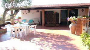 Un espace patio avec une table ronde et des chaises, un coin salon couvert et un grand vase rempli de fleurs.