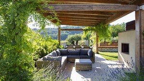 Un área de estar al aire libre con una pérgola de madera, un sofá acolchado y un banco de piedra.