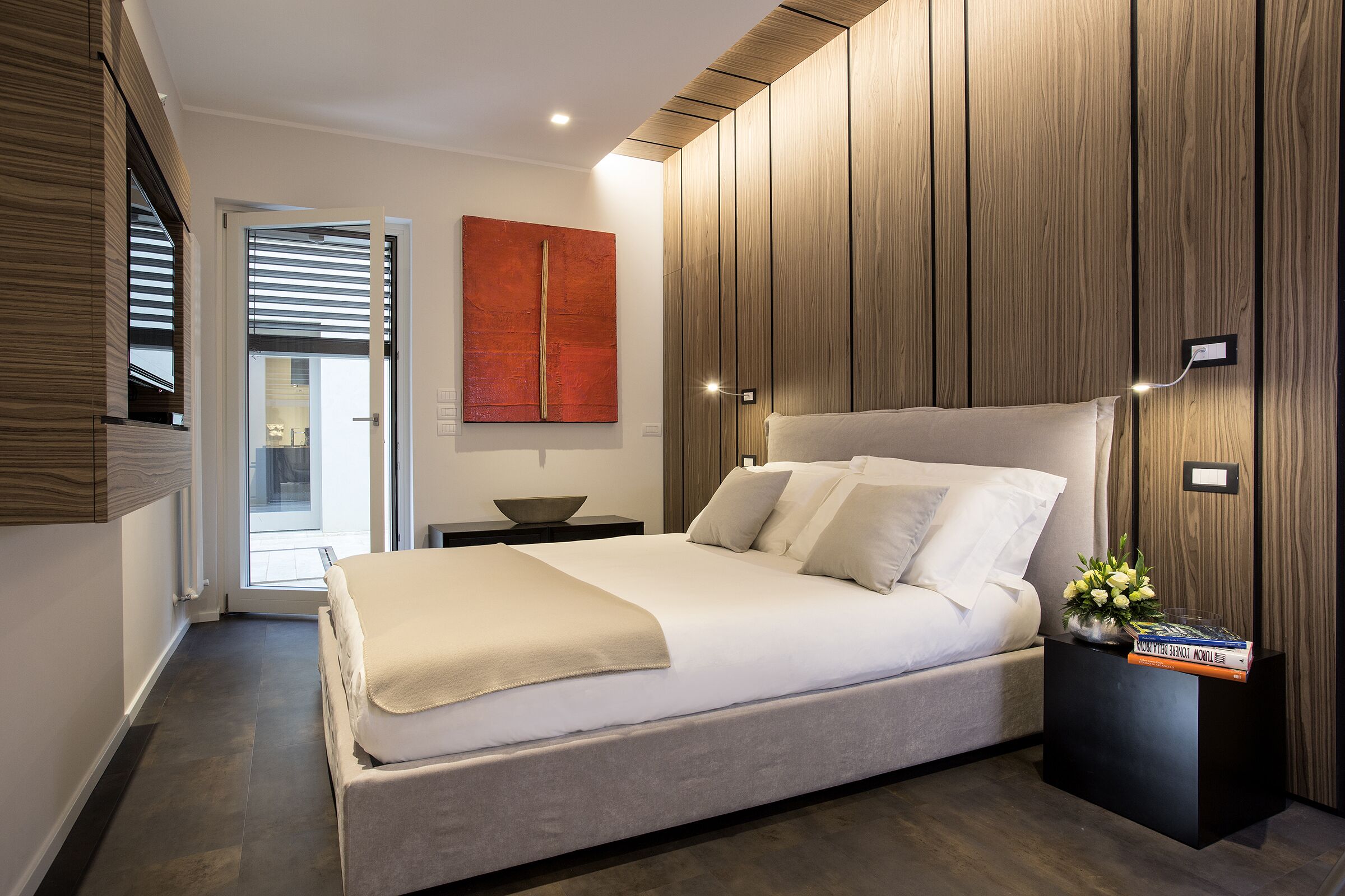 A modern bedroom with a large bed, a bedside table, and a wooden panel wall.