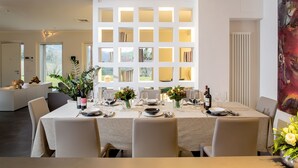 Un comedor moderno con una mesa grande dispuesta para seis personas, rodeada de sillas. Hay una planta decorativa y un florero con flores sobre la mesa.