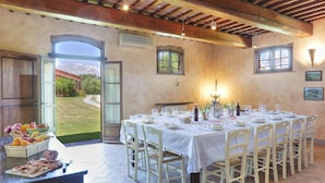Zona pranzo con tavolo apparecchiato per sei, circondato da sedie bianche, con vista su un giardino attraverso una porta aperta.