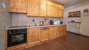 A kitchen with wooden cabinets, a built-in oven, a dishwasher, a microwave, and a countertop with various items. - Martina Ski in - Ski out 50m, Livigno, Italy (Livigno)