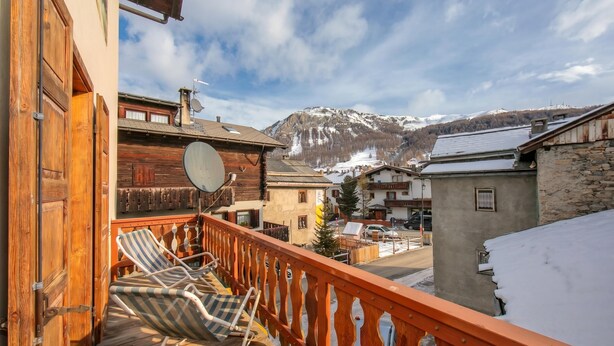A balcony with a wooden railing, a checkered lounge chair, and a view of a snow-covered mountain. - Martina Ski in - Ski out 50m, Livigno, Italy (Livigno)