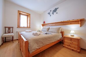 A wooden bed with a headboard, a bedside table with a lamp, and a small wooden chair.