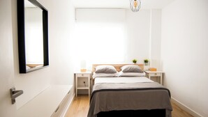 Une chambre à coucher comprenant un lit, des tables de chevet, un miroir, une fenêtre et un luminaire suspendu.