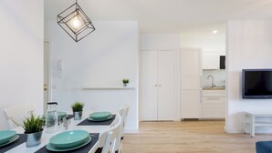 Une cuisine moderne avec des meubles blancs, un four encastré et un téléviseur fixé au mur.