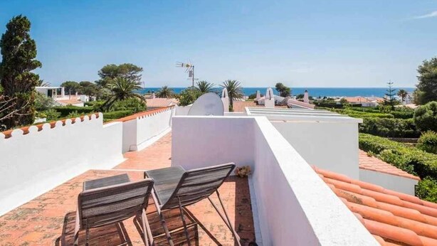 Eine Dachterrasse mit Tisch und Stühlen, mit Blick auf eine Küstenlandschaft mit Gebäuden und Bäumen.