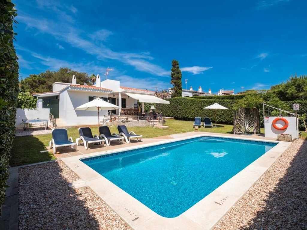 A rectangular swimming pool with a white tiled edge, surrounded by a gravel border. There are lounge chairs and umbrellas around the pool.