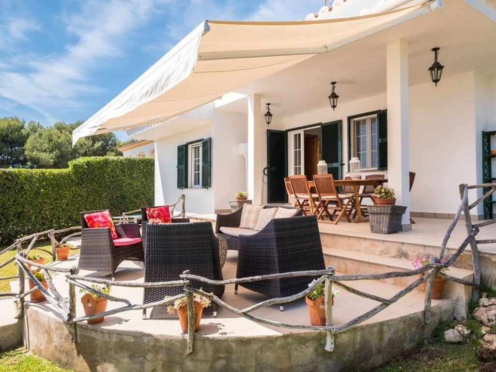 Un espace extérieur aménagé en terrasse, avec des meubles en osier, un coin salon abrité et des plantes en pot.