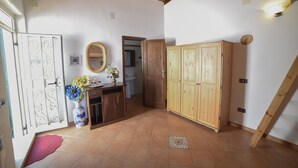 Habitació amb sostre de fusta, terra de rajola, armari de fusta, mirall i una gerra amb flors.