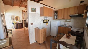 Una cuina amb armaris de fusta, un refrigerador, una placa de cocció i una zona de menjador amb taula i cadires.