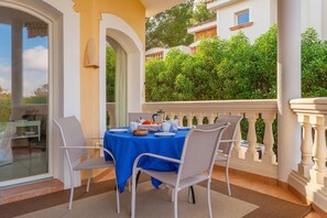 Un espace de restauration en plein air avec une table dressée pour quatre personnes, entourée de chaises blanches et recouverte d’une nappe bleue.