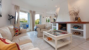 A spacious living room with a white sofa, a glass coffee table, and a fireplace.